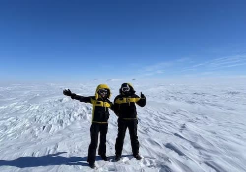 A couple of people standing on top of a snow covered slope